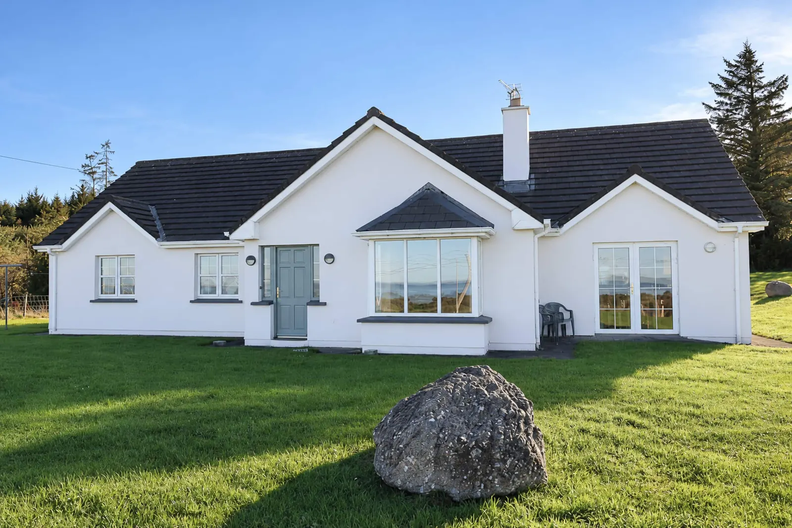 Front of Woodside House with a white facade, bay window and lawn.
