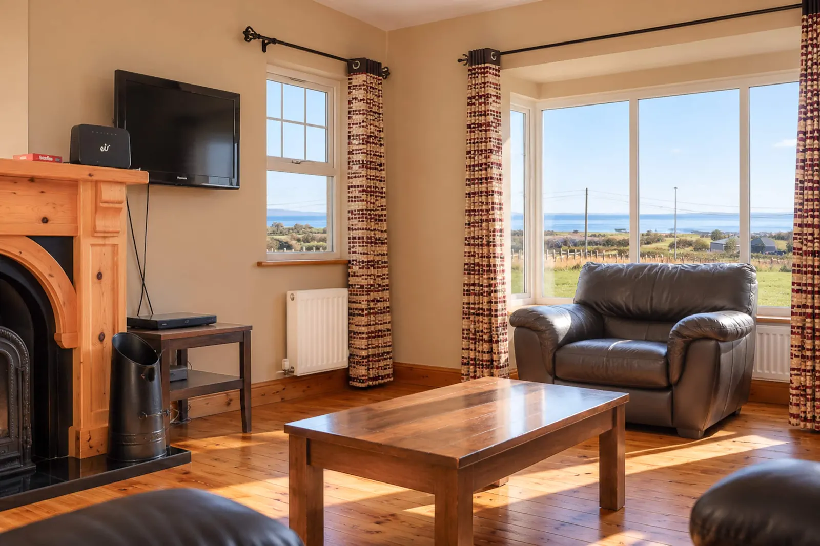 Woodside House living room with leather seating, a wooden coffee table and sea views through the bay window.