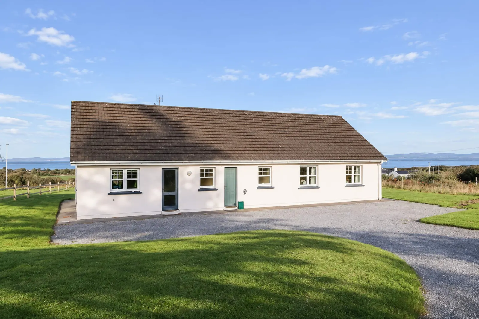 Rear of Woodside House with a gravel driveway, lawns and the sea in the distance.