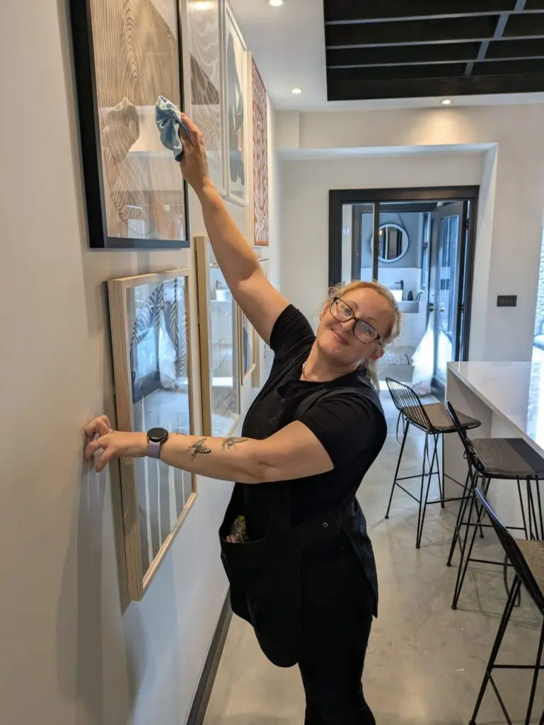 Property management cleaning. A cleaner dusting artwork on a wall. Professional cleaning services ensuring a spotless property. Interior view of a modern, well-maintained space.