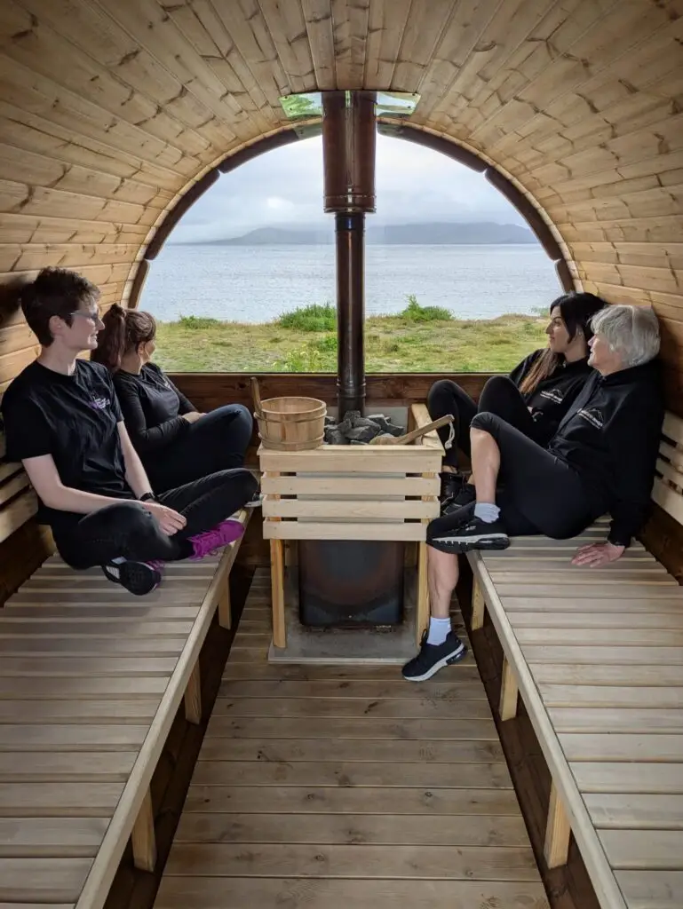 Wild Atlantic Aways team away day. Four women relaxing in a barrel sauna, with a view of the sea. Team-building activity on the Wild Atlantic Way.